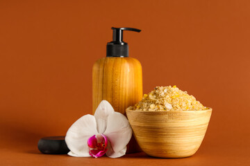 Wooden bowl with sea salt, orchid flower and bottle of cosmetic product on brown background, closeup