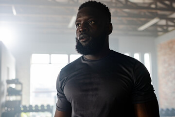 African American man wearing fitted black shirt pausing workout in studio with dumbbell rack