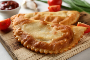 Board with tasty chebureks and fresh vegetables on white grunge table