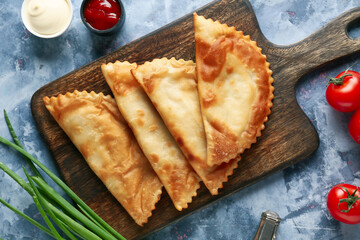 board with tasty chebureks, fresh vegetables and sauces on blue grunge table