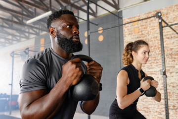Diverse workout partners performing kettlebell goblet squats in fitness studio with pull-up rig