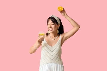 Young Asian woman with citrus infused water dancing on pink background