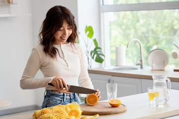 Young Asian woman making citrus infused water in kitchen