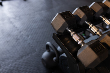 Three 15kg hexagonal dumbbells are resting on rack in gym corner, with kettlebell on rubber mat