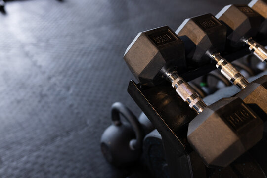 Three 15kg hexagonal dumbbells are resting on rack in gym corner, with kettlebell on rubber mat