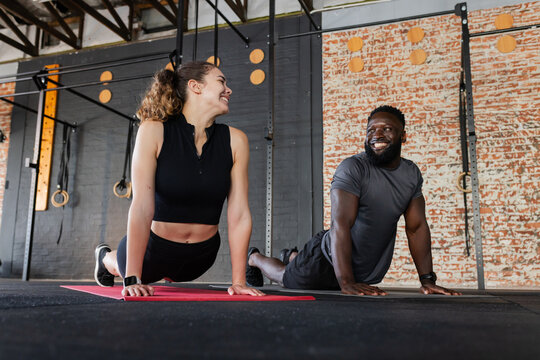Diverse workout partners stretching in cobra on red mats under metal rig rings at fitness studio