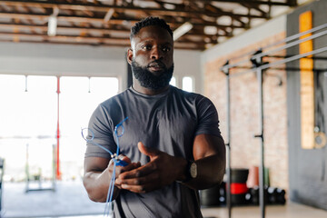 African American man wrapping blue jump rope around hands in gym wearing fitted grey athletic shirt