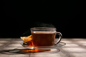 Cup of hot beverage with tea bag on grey tile table against dark wall