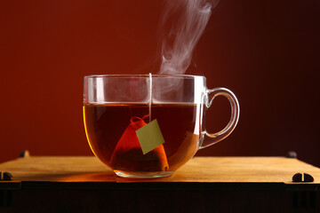 Cup of hot tea on wooden table against red wall