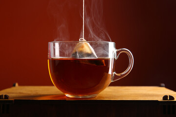 Cup of hot tea on wooden table against red wall