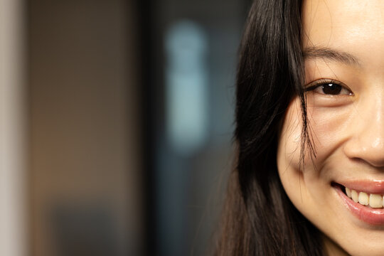 Asian woman smiling while framing face with long hair in softly lit hallway interior, copy space