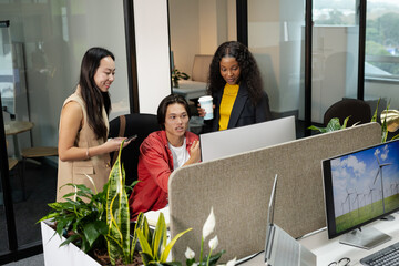 Diverse coworkers collaborating at workstation in modern office with monitor smartphone coffee cup