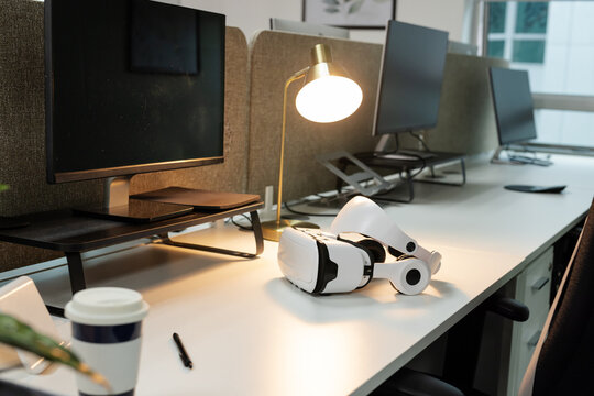 VR headset resting on desk under gold lamp casting warm light with monitors and coffee cup