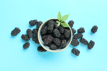 Bowl with ripe blackberry on blue background, closeup