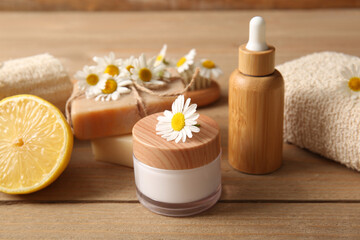 Composition with chamomile flowers, jar and bottle of cosmetic products on wooden background, closeup
