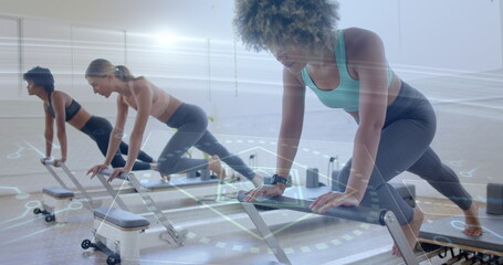 Three women performing reformer plank in Pilates studio with reformer machines and resistance bands