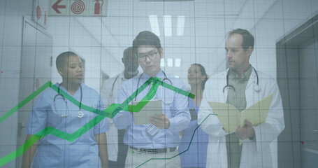 Walking medical team of five in scrubs and coats analysing data in hospital corridor, with tablet
