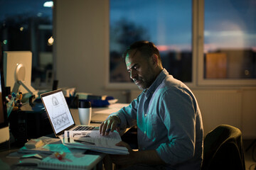 Architect working late at office looking stressed and focused on laptop