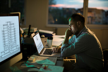 Architect working late at office looking stressed and focused on laptop