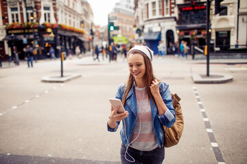 Young woman using a smart phone while crossing the street in london