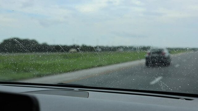 View through a car&rsquo;s front windshield with water droplets streaming upward, moved by airflow from driving. Rain or moisture creating dynamic patterns on glass