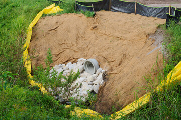 Sediment Control Basin with Erosion Prevention Measures in a Grassy Environment. Pipe outlet, rocks, silt fencing, and erosion matting, set in a natural grassy environment, showcasing effective erosio