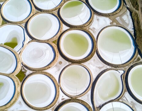 Aerial view of striking circular salt evaporation ponds creating an abstract geometric pattern with pale green water and cracked earth textures.