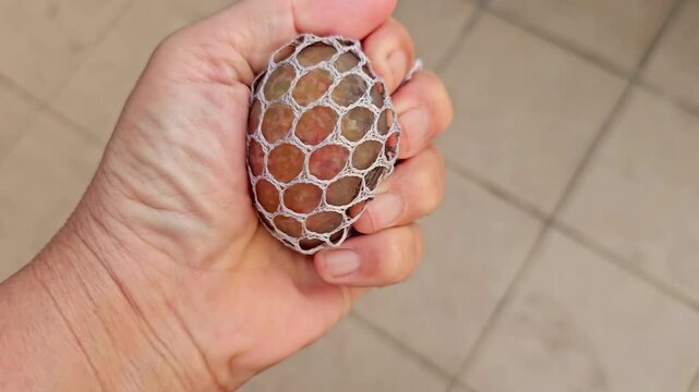 close up of right hand pressing gell type stress ball.  