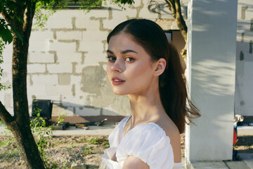 Young woman in a white dress standing outdoors, expressing serenity and confidence, surrounded by...
