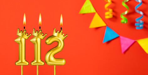 Number 112 birthday candle on an orange background with pennants
