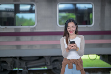 A woman is smiling and looking at her cell phone while standing next to a train
