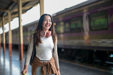 A woman wearing headphones and a backpack is walking towards a train