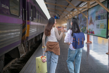 Two women are walking towards a train station with their luggage