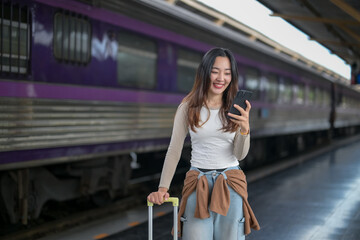 A woman is standing at a train station with a suitcase and a cell phone