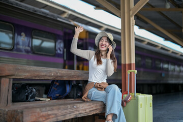 A woman is sitting on a bench at a train station, talking on her cell phone