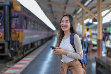 A woman is smiling and holding a cell phone while standing at a train station
