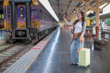 A woman is taking a selfie with her phone while standing next to a train