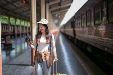 A woman is walking on a train platform with a suitcase and a cell phone