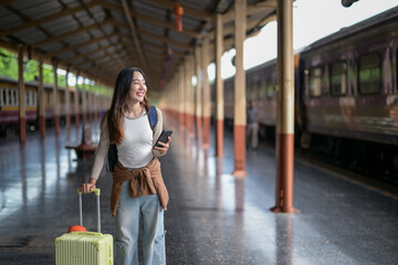 A woman is walking through a train station with a suitcase and a cell phone