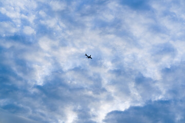Silhouette of an airplane flying through a sky full of textured clouds in soft blue and white tones.