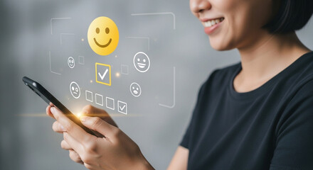 Customer service evaluation concept. A smiling Asian woman uses her smartphone and selects a smiley icon on the virtual screen to show her satisfaction.