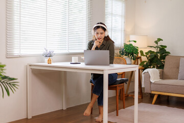 Concentrated Young Asian Female Student Engaged in Academic Research With Laptop and Headphones at...