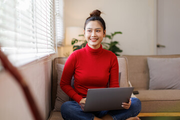Concentrated asian girl sit on couch working on laptop browsing internet at home during lazy weekend, focused young woman freelancer busy using computer surfing wireless web shopping online
