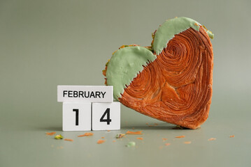 14 February wooden calendar date. Valentines day holiday Heart shaped pistachio croissant on green...