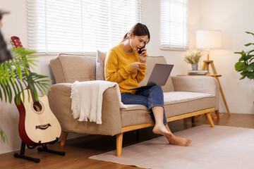 Joyful happy young Caucasian asian woman resting on sofa in apartment call on mobile phone internet...