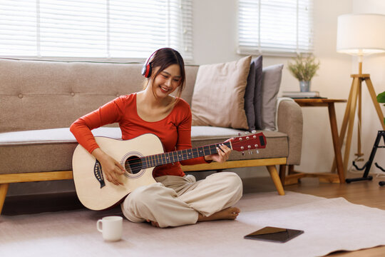 Asian young woman play guitar and produce electronic soundtrack at home. Attractive artist musician composing, create new song using musical instrument and audio equipment in recording music studio
