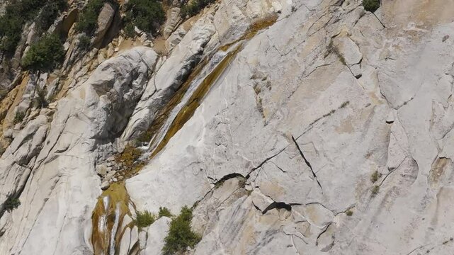 Aerial-Ascending over small waterfall down granite mountain face
