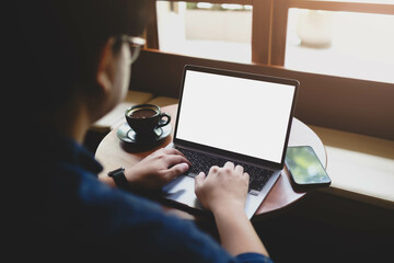 A man working on a laptop with a blank white screen by a window, with coffee and a smartphone on the desk. A perfect mockup for creative work.