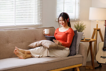 Relax Concept. Happy asian woman drinking coffee holding tablet in hand sitting on comfortable...