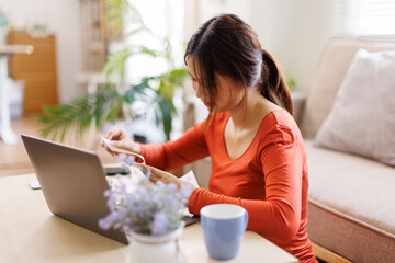Young asian woman holding pen with bills working for calculate business data, taxes, bills payment,...